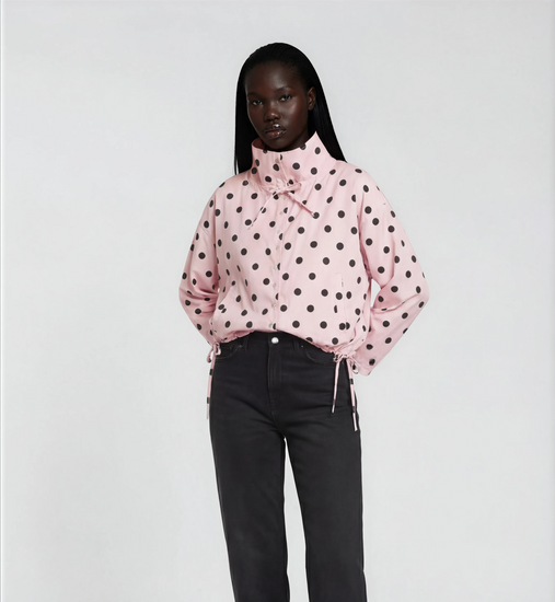 Woman wearing a pink polka dot blouse and black pants on a white background