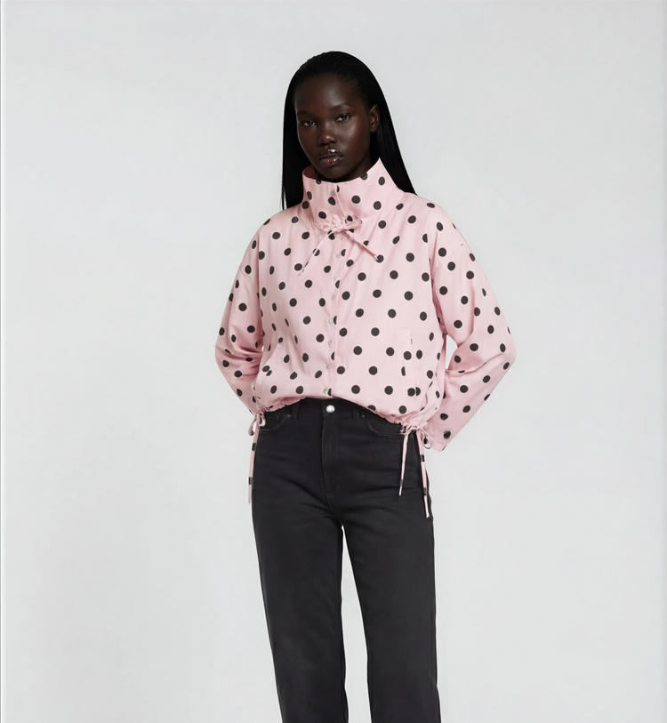 Woman wearing a pink polka dot blouse and black pants on a white background