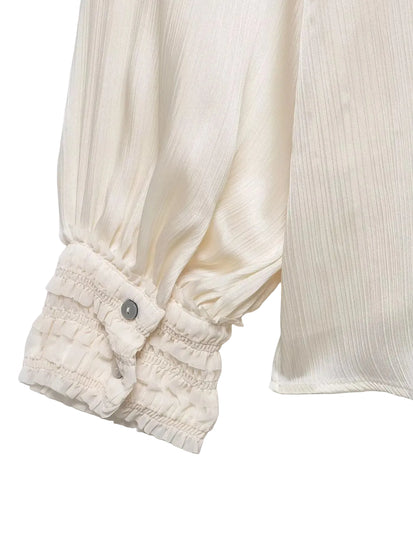 Close-up of a cream-colored blouse with smocked cuffs on a light gray background