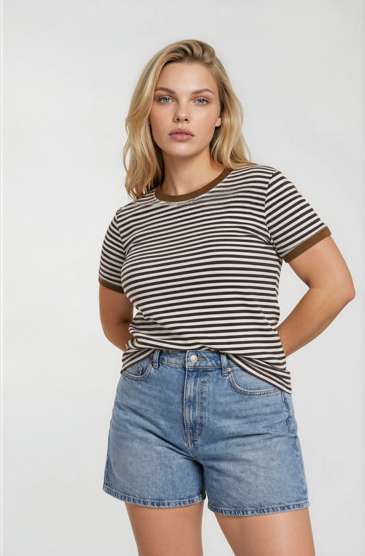 Woman wearing a brown striped short sleeve t-shirt and denim shorts on a white background